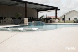 A serene outdoor pool area featuring spa loungers, a stone fountain, and a covered dining space, perfect for relaxation
