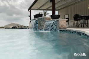 A serene pool scene featuring cascading waterfalls, a modern patio, and a distant house under cloudy skies